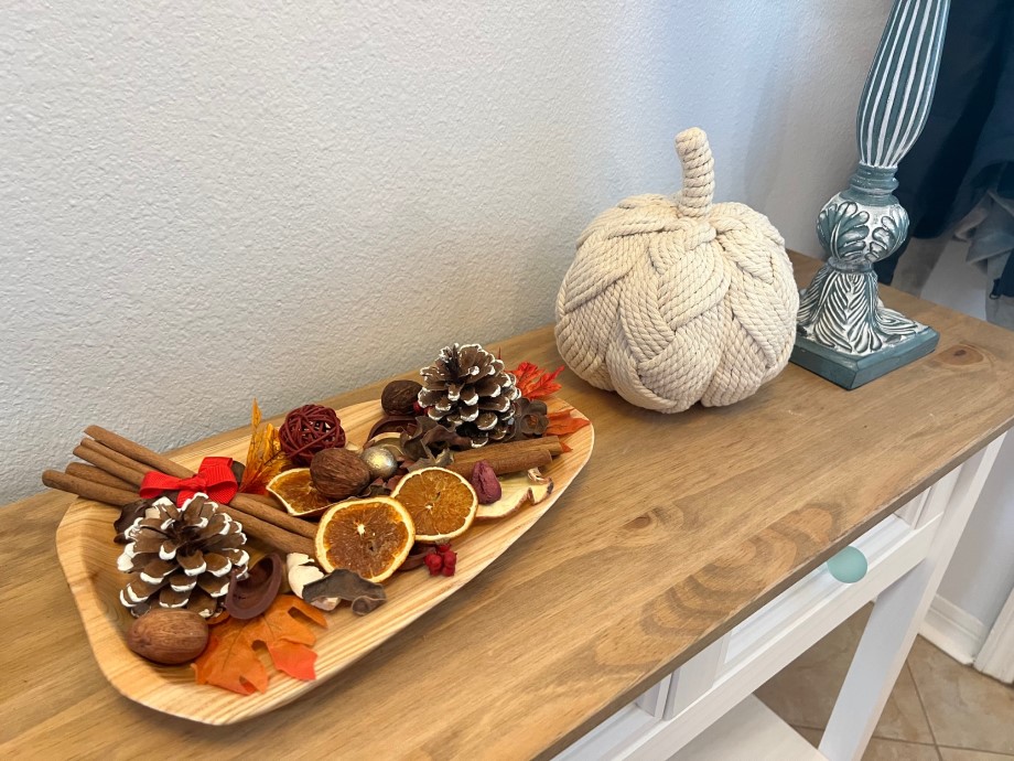 Wooden tray filled with spice sticks, dried oranges, pine cones, colorful leaves; display on entry-way counter.